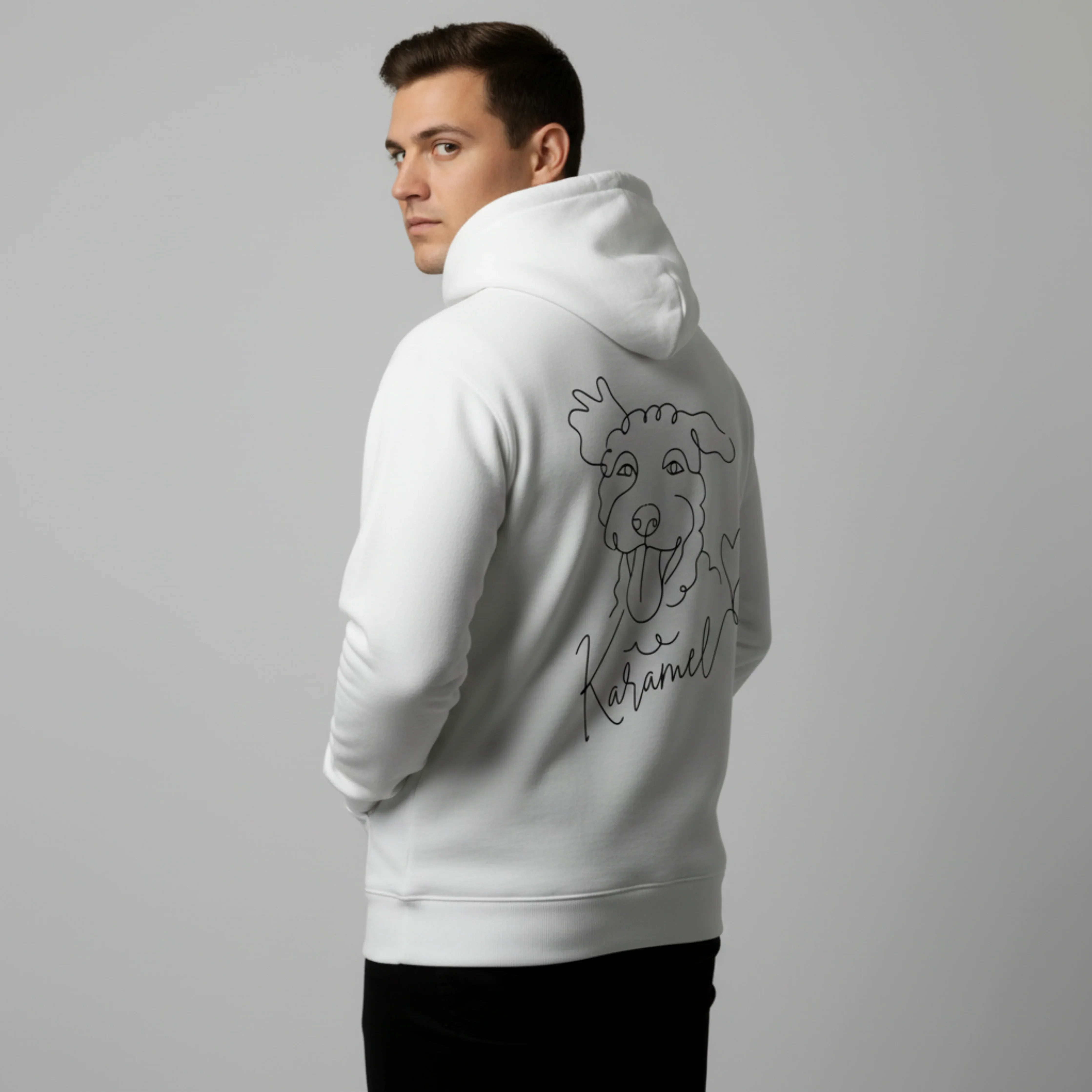 Man wearing a white hoodie with a dog illustration on the back against a gray background. Just Groom Me – Trimsalon Alphen aan den Rijn | Professional dog grooming & personalized pet apparel.